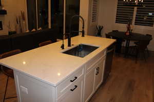 Kitchen with a kitchen bar, dark wood-style floors, white cabinetry, an island with sink, and stainless steel dishwasher