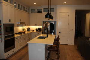 Kitchen with stainless steel appliances, a kitchen bar, a center island with sink, dark wood-style floors, and hanging light fixtures