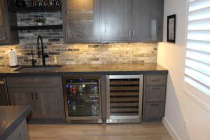 Indoor wet bar featuring beverage cooler, dark brown cabinets, light wood-style flooring, and dishwasher