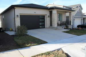 View of front of house featuring stone siding, driveway, stucco siding, and an attached garage