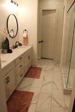 Full bath featuring double vanity, a shower stall, and light marble finish flooring