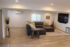 Living area with light wood finished floors, recessed lighting, and a wall unit AC