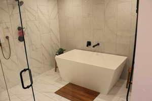 Bathroom with tile walls, a marble finish shower, a freestanding bath, and light marble finish floors