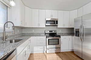 Kitchen with stainless steel appliances, white cabinets, light stone countertops, and light wood-type flooring