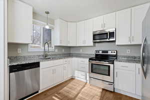 Kitchen with appliances with stainless steel finishes, white cabinetry, and light stone countertops