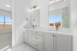 Full bath featuring double vanity, light marble finish floors, and tiled shower