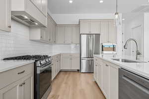 Kitchen featuring stainless steel appliances, light wood-style flooring, light stone countertops, premium range hood, and recessed lighting