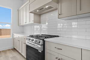 Kitchen featuring stainless steel gas range oven, custom range hood, light wood-type flooring, light stone counters, and white cabinetry