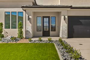 Entrance to property with a garage, a yard, concrete driveway, stucco siding, and stone siding