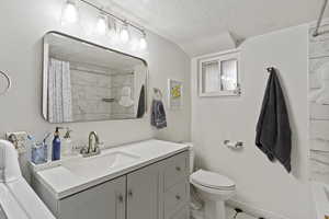 Bathroom featuring curtained shower, a textured ceiling, and vanity
