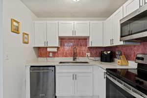 Kitchen with stainless steel appliances, white cabinets, light stone countertops, a textured ceiling, and tasteful backsplash