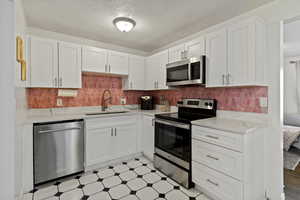 Kitchen with light floors, stainless steel appliances, white cabinets, and a textured ceiling