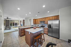 Kitchen featuring a kitchen bar, appliances with stainless steel finishes, brown cabinets, light tile patterned floors, and recessed lighting