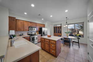 Kitchen with stainless steel appliances, brown cabinets, light countertops, hanging light fixtures, and a kitchen island