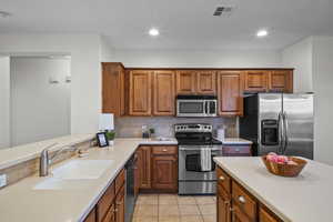 Kitchen with stainless steel appliances, brown cabinets, light countertops, tasteful backsplash, and light tile patterned flooring