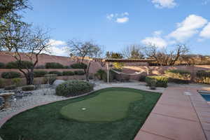 View of property's community featuring a putting area, a fenced backyard, and a patio area