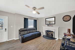 Living area featuring light wood-type flooring, a warm lit fireplace, and a ceiling fan