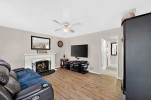 Living area with light wood-style LVP flooring, a lit fireplace, and a ceiling fan