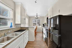 Kitchen with freestanding refrigerator, white cabinets, a chandelier, decorative light fixtures, and light wood-type flooring