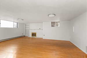 Basement featuring light wood-type flooring, a brick fireplace, wooden walls, built in features, and baseboard heating
