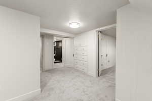 Hall featuring light colored carpet and a textured ceiling