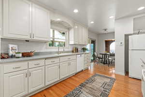 Kitchen featuring white appliances, light wood-type flooring, backsplash, recessed lighting, and white cabinets