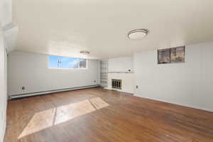 Unfurnished living room featuring a brick fireplace, baseboard heating, wood walls, hardwood / wood-style flooring, and built in features