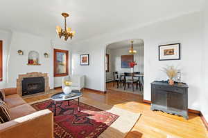 Living area featuring arched walkways, a chandelier, light wood-type flooring, and a fireplace with raised hearth