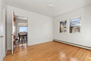 Unfurnished room featuring a baseboard heating unit, light wood finished floors, and arched walkways