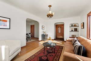 Living room with wood finished floors, built in features, arched walkways, and a chandelier
