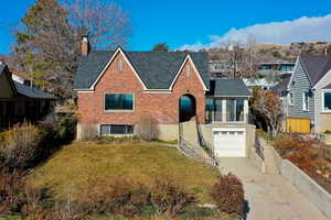 View of front of property featuring brick siding, a chimney, a front yard, driveway, and a garage