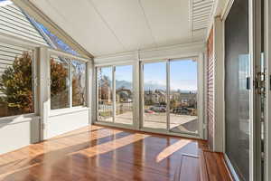 Unfurnished sunroom featuring lofted ceiling, wood finished floors, a residential view, and a mountain view