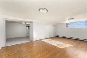 Unfurnished bedroom featuring light wood-type flooring, a baseboard heating unit, and a closet