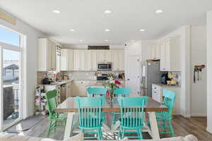 Kitchen with appliances with stainless steel finishes, backsplash, light stone counters, light wood-type flooring, and recessed lighting