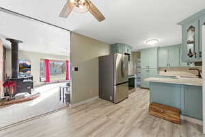 Kitchen featuring a wood stove, appliances with stainless steel finishes, light countertops, green cabinetry, and light wood-type flooring