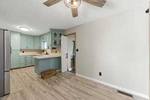Kitchen featuring glass insert cabinets, green cabinetry, light countertops, freestanding refrigerator, and light wood-style flooring
