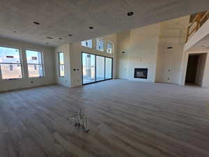 Unfurnished living room featuring a glass covered fireplace, wood finished floors, and a towering ceiling