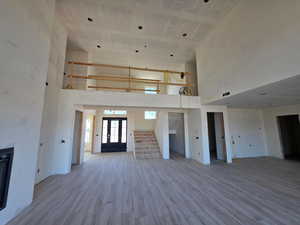 Unfurnished living room with a towering ceiling, stairs, wood finished floors, french doors, and a glass covered fireplace