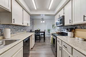 Kitchen with stainless steel appliances, tasteful backsplash, light wood finished floors, and a chandelier