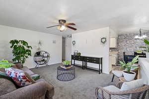 Living room featuring light carpet, a chandelier, a ceiling fan, and a textured ceiling