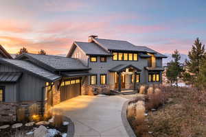 Modern inspired farmhouse featuring concrete driveway, stone siding, an attached garage, a chimney, and board and batten siding
