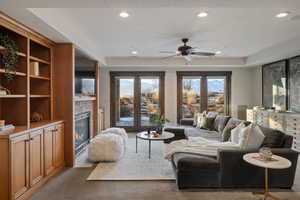 Living room featuring light colored carpet, a glass covered fireplace, a ceiling fan, and recessed lighting