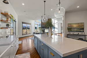 Kitchen with blue cabinets, open floor plan, light stone countertops, open shelves, and hanging light fixtures