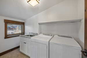 Washroom with lofted ceiling, washer and clothes dryer, cabinet space, light tile patterned floors, and a textured ceiling