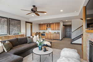 Living room with light colored carpet, stairs, recessed lighting, a glass covered fireplace, and a ceiling fan
