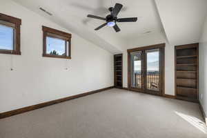 Carpeted spare room featuring built in features, healthy amount of natural light, ceiling fan, and vaulted ceiling