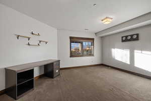 Unfurnished office with dark colored carpet and a textured ceiling
