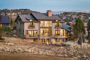 Back of house with a balcony, a chimney, board and batten siding, and stone siding