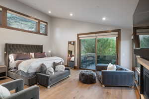 Bedroom featuring access to exterior, recessed lighting, light wood-style floors, a fireplace, and lofted ceiling