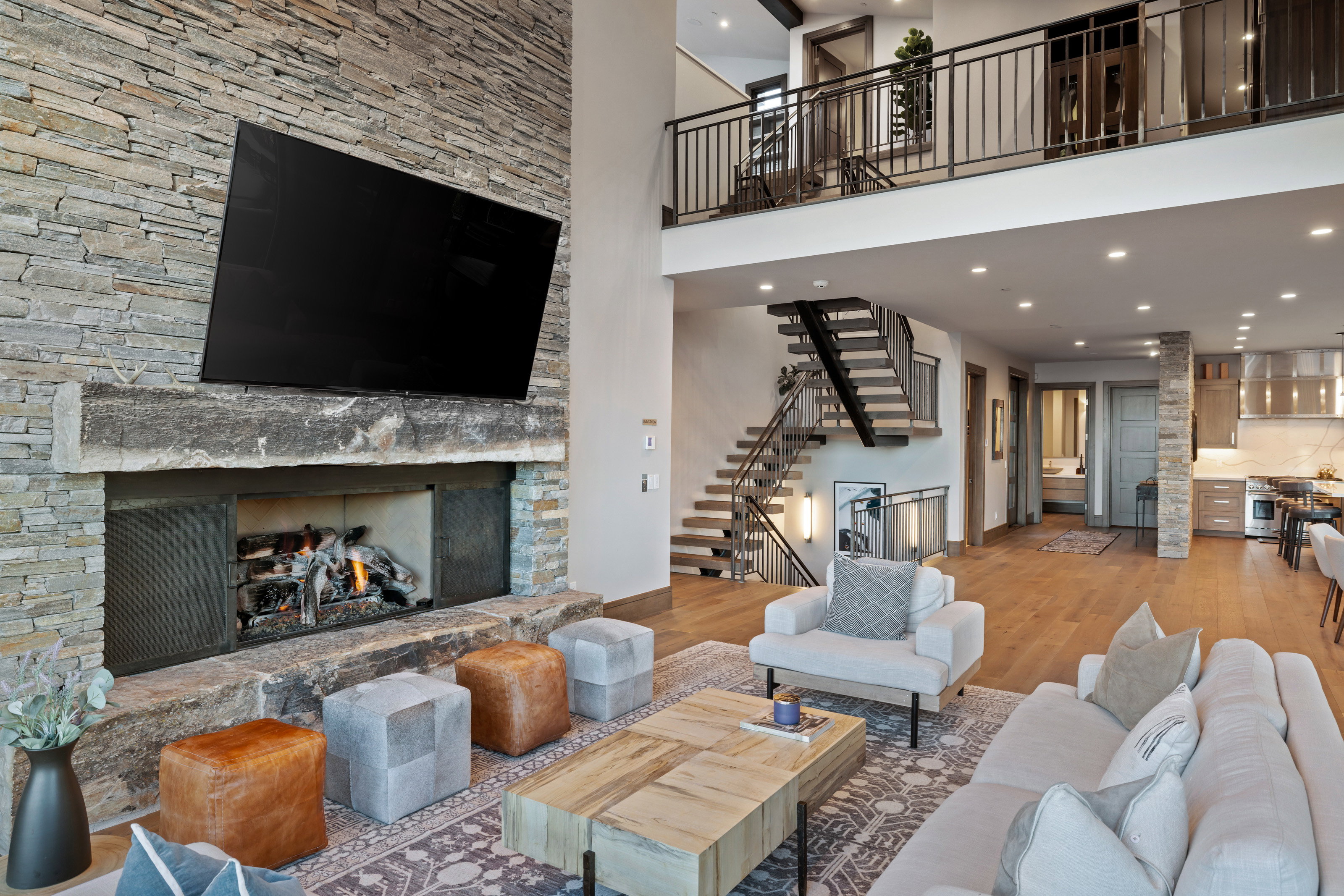 Living room with wood finished floors, a stone fireplace, recessed lighting, stairs, and a towering ceiling